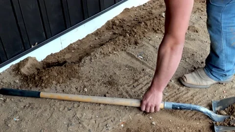 Working man uses flat shovel or spade to move dirt near a house foundation. Stock Footage 153862057