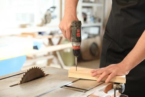 Working man using electric screwdriver at carpentry shop, closeup. Space for  Stock Photos