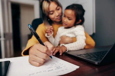 Working mom writing notes while holding her daughter Stock-Fotos