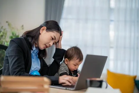 Working mother multitasks with baby while struggling to meet deadlines in a.. Stock Photos