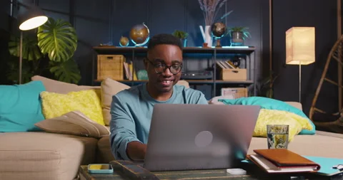 WORKING ONLINE Young happy smart black freelance businessman in eyeglasses using Stock Footage 169668786