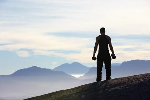 Working out with a view. Rearview of a man standing on a mountain top holding Stock Photos