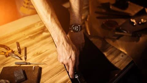 Working process of the leather belt in the leather workshop. Man holding tool Stock Photos