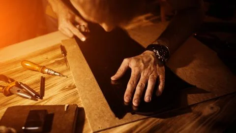 Working process of the leather belt in the leather workshop. Man holding tool Stock Photos