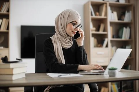 Working process at office of young serious muslim girl having phone call with Stock Photos