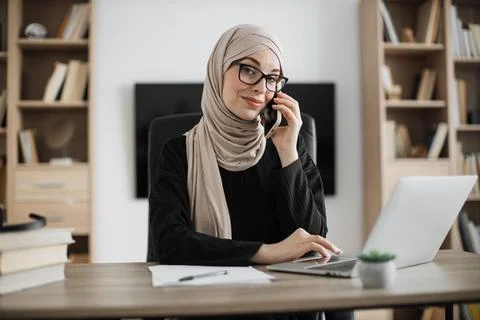 Working process at office of young serious muslim girl having phone call with Fotos de archivo