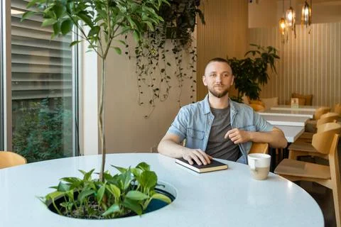 Working remotely while sitting at a round table in a modern cafe with plant.. Stockfoto's