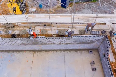 Working on scaffolding, mason constructs a concrete wall with cement blocks Foto stock