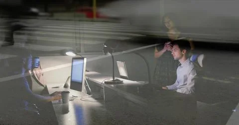 Working seated man wearing button-up shirt checking dual monitors at dim office, Stock Photos