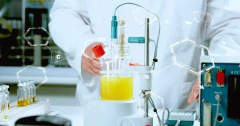 Working senior chemist in lab coat adjusting glass reactor with yellow liquid at Stock Photos