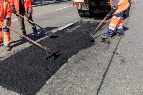 The working team evenly distributes part of the asphalt with shovels during r Stock Photos