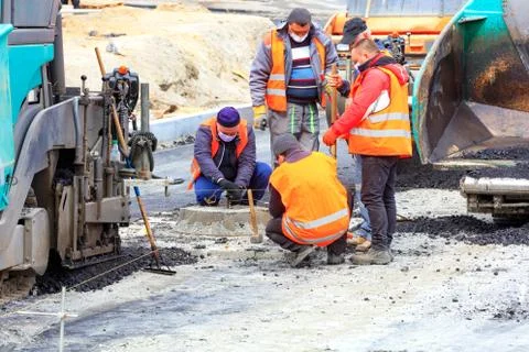 The working team of road workers in protective masks sets the necessary level Stock Photos