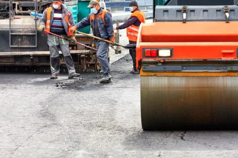 The working team of road workers in protective medical masks and overalls lay Stock Photos