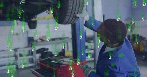 Working tech reaching lifted tire in shop wearing blue coverall gloves binary Foto stock