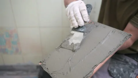 The working tiler applies glue on the tile with a notched trowel before gluing Stock Footage 199583134