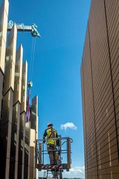 Workman hoisted using a mechanical crane to a high level to inspect shade Stock Photos