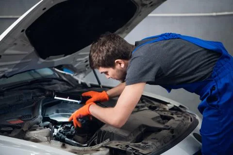 A workman inspects a automobile engine using a flashlight Stock Photos