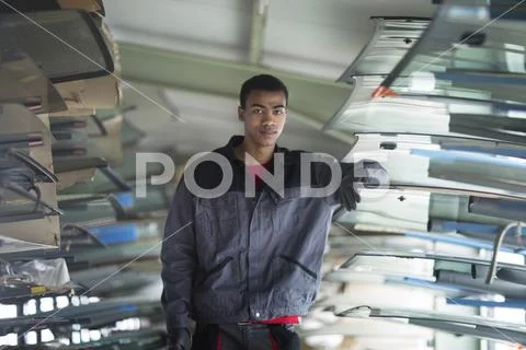 Workman leaning against stack of car windshield in workshop Stock Photos