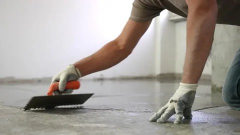 Workman pouring self-leveling screed on floor, spreading it and smoothing with Video stock 148993793