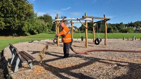 Workman replacing soft woodchip on a children's playground Stock Footage 284555976