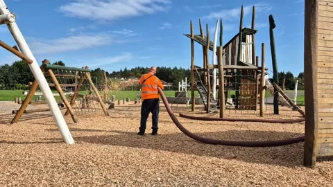 Workman replacing soft woodchip on a children's playground Stock Footage 284556011