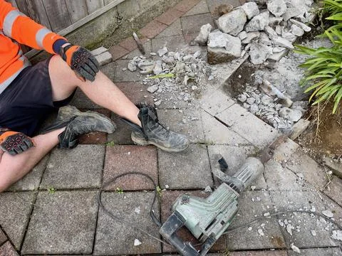 Workman sitting down having a rest after using a concrete breaker to demolish pa Stock Photos