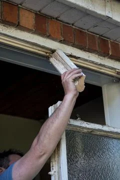 Workman using his hand and arm to remove part of an old wooden window frame Stock Photos