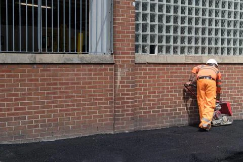 Workman using a plate vibrator to compact tarmac pavement siewalk. Stock Photos