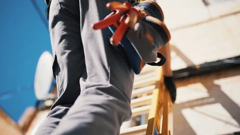 Workman Wearing High Visibility Clothing and Tool Belt Climbing a Ladder - Stock Footage