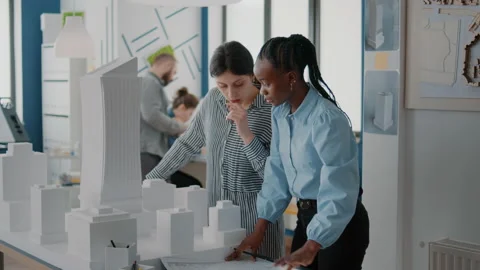 Workmates analyzing blueprints plan and building model on table, working on 스톡 동영상 166423542