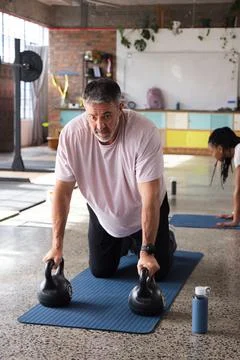 Workout classmates with middle-aged man kneeling on blue mat gripping two Stock Photos