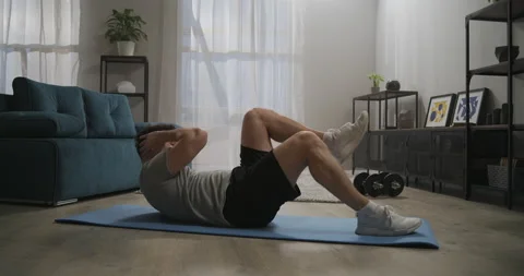 Workout at home, man is lying on floor, lifting torso and legs, exercise for Stock Footage 147927089