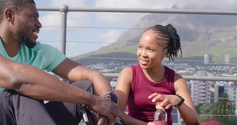 Workout partners sitting rooftop, woman fidgeting cap, opening pink bottle, man Stock Footage 340674792