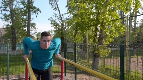 Workout. Young athlete performs push-ups on the uneven bars in the morning Stock Footage 84492826