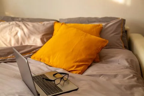 Workplace in bed. Laptop with glasses on the bed on gray bedding and yellow Stock Photos