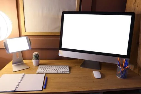 Workplace with blank computer and glowing lamp in dark office Stock Photos