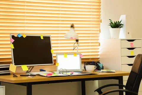 Workplace with blank laptop, computer and sticky notes near window in office Stock Photos