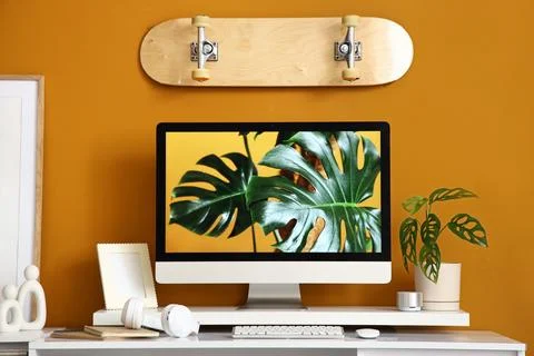 Workplace with computer and skateboard on orange wall in office Stock Photos