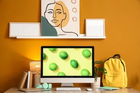Workplace with computer, backpack and shelf on orange wall in office Stock Photos