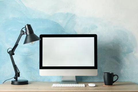 Workplace. Computer with empty screen and cup on wooden table. Light blue bac Stock Photos