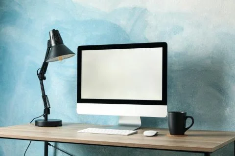 Workplace. Computer with empty screen and cup on wooden table. Light blue bac Foto stock