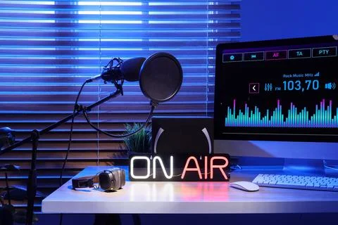 Workplace with computer, glowing ON AIR sign and microphone in dark radio stu Stock Photos