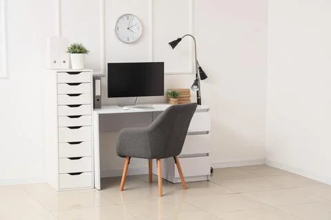 Workplace with computer, lamp and clock on light wall in office Stock Photos