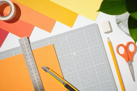 Workplace with cutting mat, scissors, craft knife, orange paper and tools o.. Фото