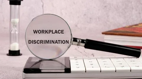 WORKPLACE DISCRIMINATION word concept through a magnifying glass on a gray wa Stock Photos