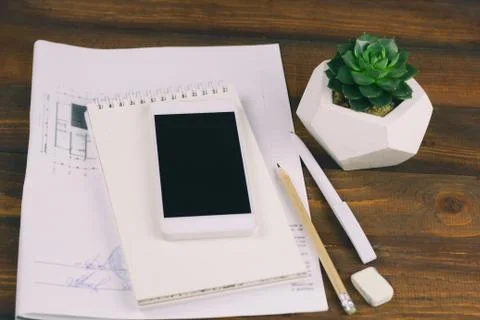 Workplace with drawing plan, notepad, phone with blank black screen, pen, pen Stock Photos