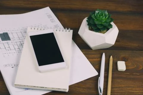 Workplace with drawing plan, notepad, phone with blank black screen, pen, pen Stock Photos