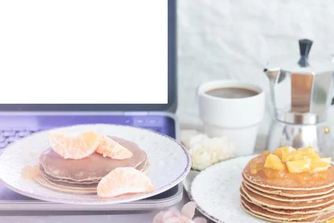 Workplace. Laptop with blank screen on table with breakfast: pancakes and cof Stock Photos