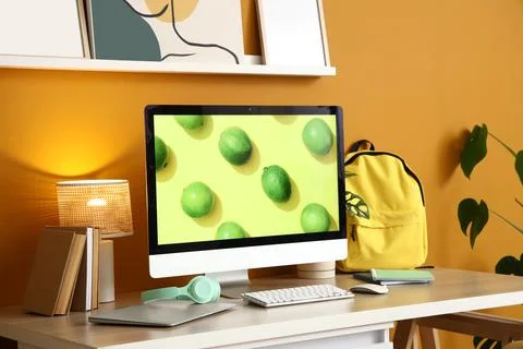 Workplace with modern gadgets, backpack and glowing lamp near orange wall in  Stock Photos
