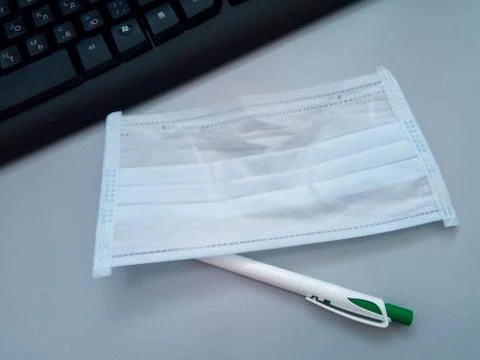 Workplace near the computer, on the table is a used medical mask and ballpoin 스톡 사진
